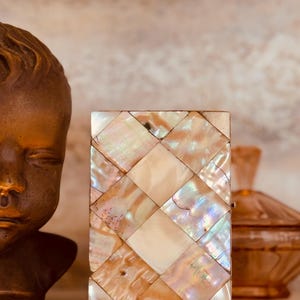 May include: Rectangular box with a mother-of-pearl mosaic pattern. The iridescent tiles are arranged in a diamond pattern, with a central diamond shape. The box is a mix of cream, white, and iridescent colors.