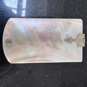 May include: A rectangular case with a curved top edge, crafted from iridescent mother-of-pearl with swirling pink and white tones. The case features a silver-toned metal hinge on the right side and a small circular silver-toned metal snap closure.