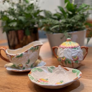 May include: A set of three vintage ceramic serving dishes with a floral design. The dishes are white with brown, green, and pink floral accents. The dishes are in the shape of leaves and flowers.