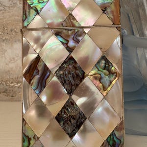 May include: A rectangular box with a hinged lid, decorated with a mosaic of iridescent abalone shell tiles in a diamond pattern. The shell pieces show colours of white, pink, green, and brown.