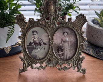 A solid heavy cast brass ornate vintage double frame with oval apertures with glass holding 2 original Victorian photos