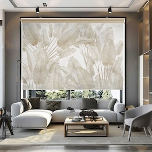 Op de afbeelding: Een moderne woonkamer met een witte hoekbank en een salontafel. Het raam is bedekt met een beige rolgordijn met een aquarelprint van grote tropische bladeren.