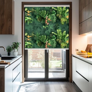 Könnte beinhalten: Ein weißer Fensterrollo mit tropischem Muster aus grünen Blättern und orangefarbenen Blüten. Der Rollo ist teilweise hochgezogen und gibt den Blick auf einen Garten frei.