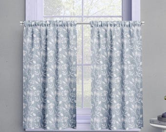 May include: Two light blue window curtains with a white floral pattern. The curtains are hanging on a silver rod in front of a window. The floral design includes leaves and small flower clusters.