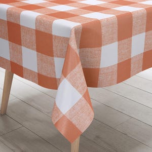 Puede incluir: Mantel de mesa a cuadros naranja y blanco con textura tejida. El mantel está drapeado sobre una mesa de madera con patas de madera.