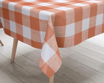 May include: Orange and white checkered tablecloth with a woven texture. The tablecloth is draped over a wooden table with wooden legs.