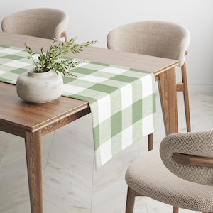 May include: A green and white checkered table runner on a wooden table with two chairs. The table runner is made of fabric and has a farmhouse style.