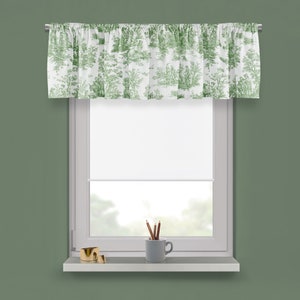 May include: A white valance with a green toile pattern hangs over a window with a white roller shade. A gold metal decorative ring and a gray ceramic mug with pencils are on the window sill.