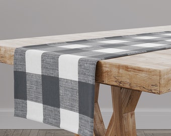 May include: A black and white checkered table runner with a woven texture. The runner is laying on a wooden table with a natural finish.
