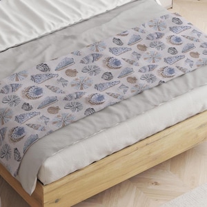 May include: A white bed with a light blue and brown patterned bed runner featuring a seashell design. The bed has a wooden frame.