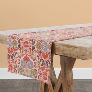 May include: A red, orange, green, and gray floral table runner with a paisley pattern. The runner is on a wooden table.