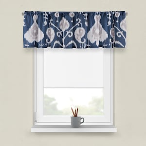 May include: A blue and white patterned valance with a ruffled edge hangs above a window with white trim. A white window blind is partially lowered. A small gray cup with brown pencils sits on the window sill.