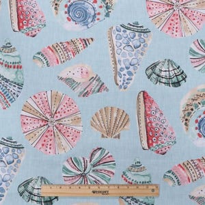 May include: Light blue fabric featuring a repeating pattern of colorful seashells. The seashells are in various shapes and sizes, with pink, blue, green, and tan hues. A wooden ruler with inch markings is at the bottom.
