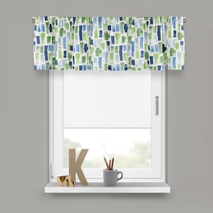 May include: A window valance with a white background and a pattern of blue and green brushstrokes. The valance is mounted above a white window with a white roller shade. A shelf below the window holds decorative items.