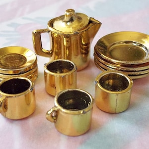 May include: A miniature gold tea set with a teapot, four cups, and four saucers. The set is made of shiny gold metal and has a classic design.