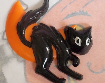 May include: Black plastic Halloween cat figurine with orange crescent moon. The cat is in a crouching position with its tail curled around the moon.