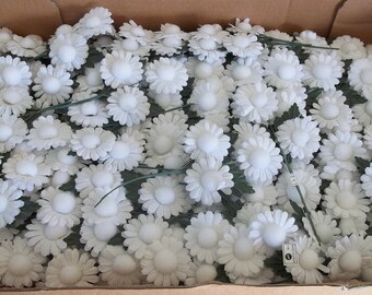May include: A box filled with white artificial daisy flowers with green stems. The flowers are arranged in a random pattern.