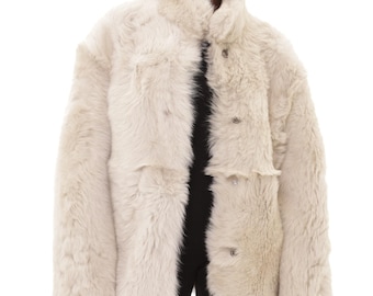 May include: A cream-colored faux fur jacket with a high collar and button closures. The jacket has a slightly oversized fit and features two front pockets. The model is wearing a black top and black pants.