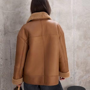 Puede incluir: Chaqueta de borreguillo marr&oacute;n con cuello y pu&ntilde;os de borreguillo beige. La chaqueta tiene un dise&ntilde;o cl&aacute;sico con costuras visibles y un corte relajado. El modelo lleva vaqueros oscuros.