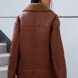 Puede incluir: Chaqueta de cuero marr&oacute;n con cuello de borrego. La chaqueta tiene un corte holgado y presenta detalles de costura visibles. El modelo lleva la chaqueta con pantalones negros. Una opci&oacute;n de abrigo c&aacute;lida y elegante.