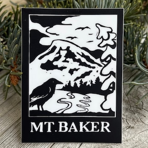 May include: Black and white sticker with a silhouette of a mountain, trees, a river, and a crow. The text "MT. BAKER" is at the bottom of the sticker.
