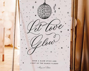 May include: A white sign with the words "Let Love Glow" in elegant script, featuring a disco ball illustration. The sign is on a gold metal stand, with text that reads "Grab a glow stick and light up the dance floor!"
