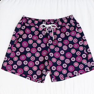 May include: Navy blue swim shorts with a repeating pattern of pink and white circular designs. The shorts have a white drawstring and are made of a lightweight fabric. The shorts are designed for swimming and other water activities.