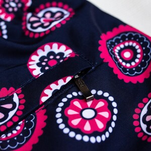 May include: Close-up of navy blue fabric with a repeating paisley pattern in pink, white, and black. A small pocket with a metal zipper is visible. The fabric has a slight sheen.