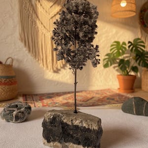 May include: A miniature decorative tree with grey leaves and a brown trunk, set in a natural stone base. The stone has a dark grey and beige layered appearance. A unique home decor item.