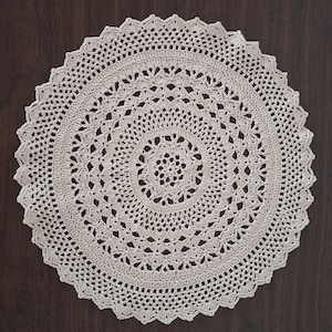 May include: A white crocheted doily with a delicate, intricate pattern. The doily is circular and has a scalloped edge.