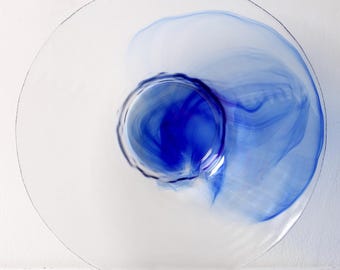 Op de afbeelding: Een heldere glazen plaat met een blauw swirl-ontwerp. De swirl is geconcentreerd in het midden van de plaat en vervaagt naar de randen.