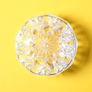 Könnte beinhalten: Eine klare Glasschüssel mit einem dekorativen Sternmuster. Die Schüssel befindet sich auf einem gelben Hintergrund.