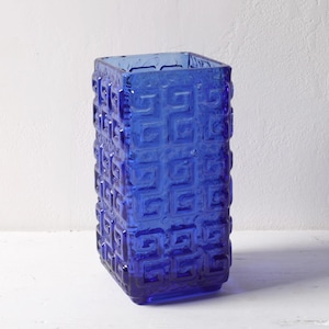 Può includere: Un vaso in vetro blu cobalto con un motivo geometrico. Il vaso è di forma rettangolare e ha una superficie testurizzata.