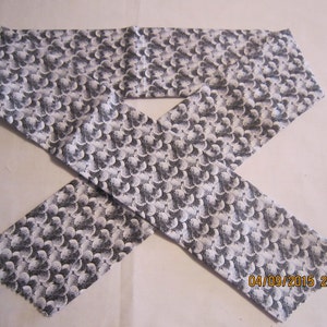 May include: A white fabric headband with a black and white pattern of small circles. The headband is folded in half and tied in a knot.