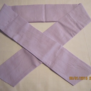 May include: A light purple fabric sash or belt, folded and tied in a knot. The fabric has a slightly textured surface.
