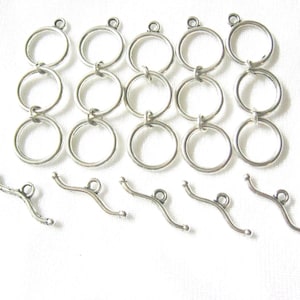 May include: Five silver-toned metal toggle clasp sets, each consisting of a vertical chain of three interconnected circular rings and a separate curved bar component with a central loop, arranged in rows on a plain white surface.