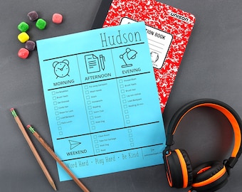 May include: A blue daily routine checklist labeled "Hudson" with morning, afternoon, and evening sections. A red composition notebook, pencils, headphones, and colorful candies are also in the image.