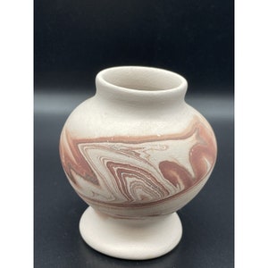 May include: A small, white ceramic vase with a brown and red marbled design. The vase has a round body and a flared base.