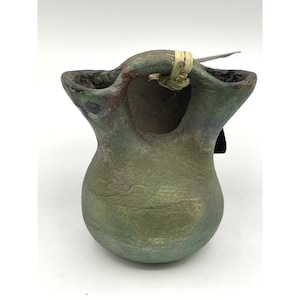 May include: A small, green, ceramic pot with a unique, abstract design. The pot has two openings at the top and a small hole on the side.