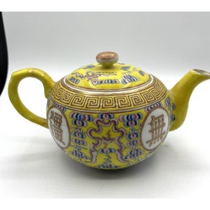 May include: A yellow porcelain teapot with a round body and a lid. The teapot is decorated with a gold and red floral pattern and Chinese characters. The characters on the teapot read "福" and "祿".