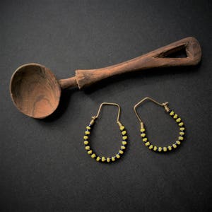May include: A pair of gold hoop earrings with yellow and black beads. The earrings are on a dark background.