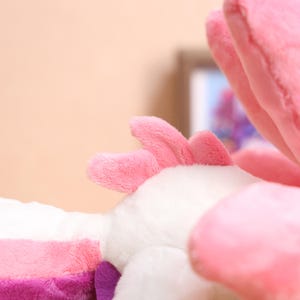 May include: Close-up of a pink and white plush toy with a pink ear. The toy is made of soft, fluffy material.