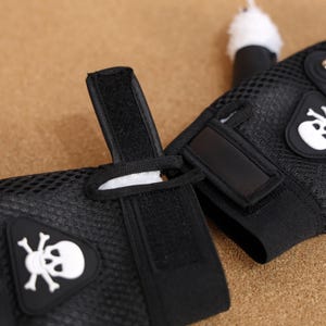 Puede incluir: Un par de guantes sin dedos de malla negra con un dise&ntilde;o de calavera y huesos cruzados blancos. Los guantes tienen correas de velcro ajustables.