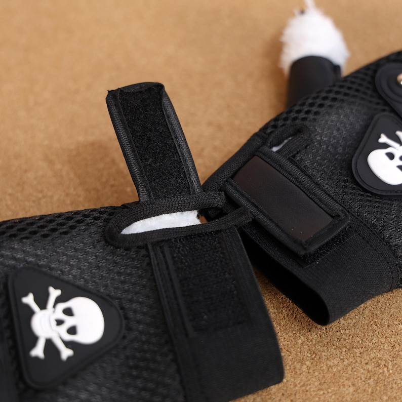 Puede incluir: Un par de guantes sin dedos de malla negra con un dise&ntilde;o de calavera y huesos cruzados blancos. Los guantes tienen correas de velcro ajustables.