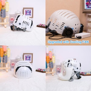 May include: White safety helmet with a built-in fan for cooling. The helmet has a mesh design and a black strap. The fan is powered by a battery pack that is not visible in the image. The text "Upgraded with Cooling FAN" is visible below the helmet.