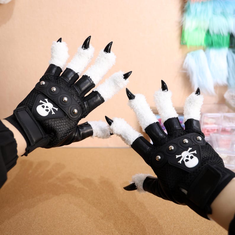 Puede incluir: Un par de guantes negros sin dedos con garras de piel blanca y detalles de calavera. Los guantes tienen tachuelas met&aacute;licas y un dise&ntilde;o de malla.
