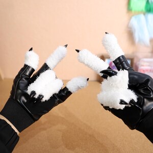 Puede incluir: Un par de guantes de cuero sint&eacute;tico negro con garras blancas y peludas. Los guantes tienen un pu&ntilde;o en la mu&ntilde;eca y est&aacute;n dise&ntilde;ados para parecer patas de animales.