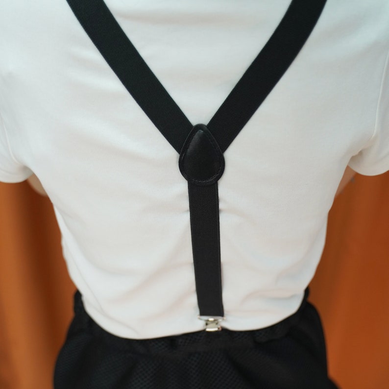 May include: A white t-shirt with black suspenders. The suspenders have a black leather adjustable buckle.