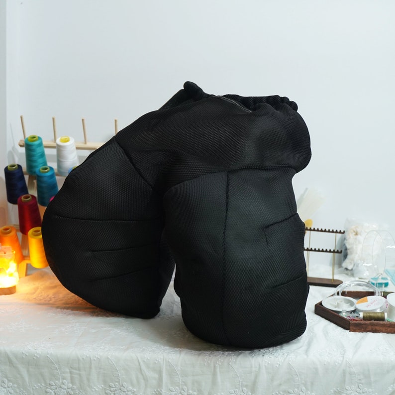 May include: A black mesh pillow with two rounded sections. The pillow is designed to provide support for the back and neck.
