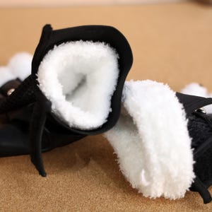 Puede incluir: Primer plano del interior de dos botas negras con forro de piel sint&eacute;tica blanca. Las botas est&aacute;n hechas de un material suave y texturizado.